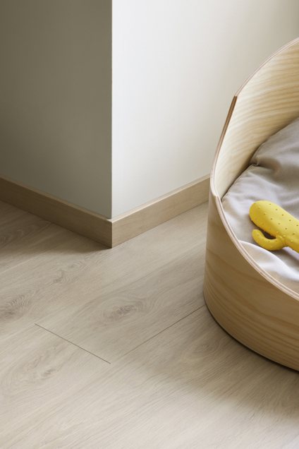 Bordshörn med ljus trägolv, beige vägg, rund träbädd med grå kudde och gul leksak.