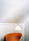 Orange stol, golvlampa med skärm i hörn av rum med ljusa väggar och tak i vita paneler.