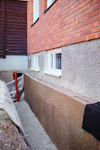 Röd tegelvägg med synlig källargrund och isoleringsskivor intill. Grus längs basen av byggnaden.