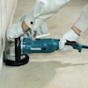 En person slipar ett betonggolv nära en vägg med en blå Makita betongslipmaskin.