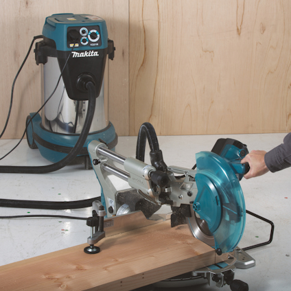 Cirkelsåg med pågående sågning av träbit, ansluten till en Makita dammsugare. En hand håller träbiten.