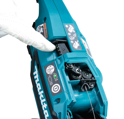 Handskbeklädd hand som justerar en blå och svart Makita-najmaskin, med synliga knappar och mekaniska delar.