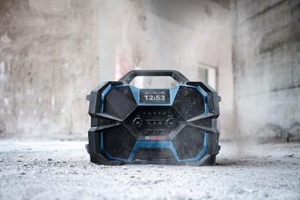 Bärbar radio på dammig golvyta, visande klockan 12:53. Robust design med blå och svarta detaljer.