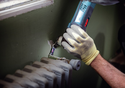 Person i skyddshandske använder ett elektriskt verktyg nära ett fönster och ett element.