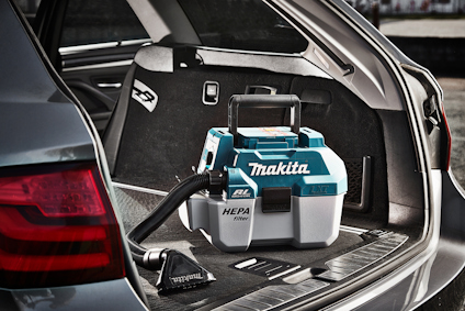 Bärbar dammsugare med HEPA-filter märkt "Makita" placerad i bagageutrymmet på en bil.