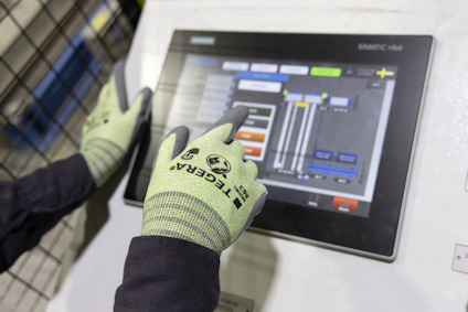 Händer med gröna handskar använder en pekskärm med olika symboler och knappar. Skärmen visar "SMARTC HMI".