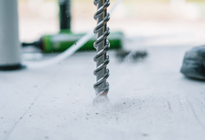 En borr av metall borrar i en betongyta, vilket orsakar damm och små partiklar i luften.