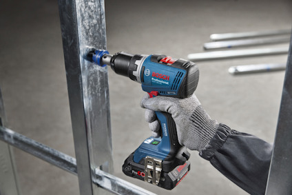 En person borrar i en metallram med en blå, batteridriven borrmaskin. En hand klädd i arbetshandske håller borren.