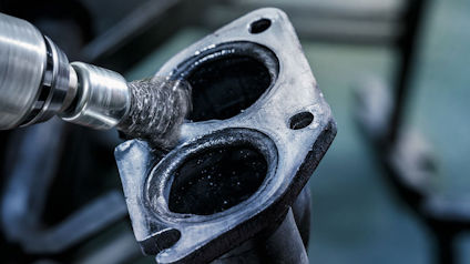 Närbild på en borrmaskin som bearbetar en metallkomponent med två hål.