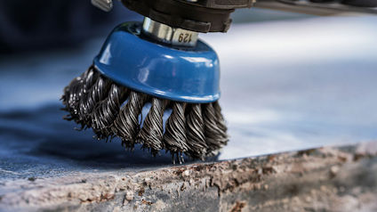 Roterande stålborste med blått fäste polerar kant på metallplatta.