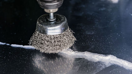 Roterande stålborste slipar en metallyta med en vit spricka.