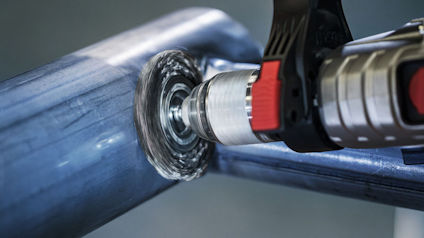 En borr med stålborsthuvud polerar en silverfärgad metallrörs yta.