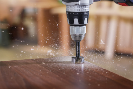 Borrmaskin borrar ett hål i trä med träspån som flyger runt.