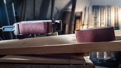 Slipmaskin och slipband placerade på en träbänk i en verkstadsmiljö.