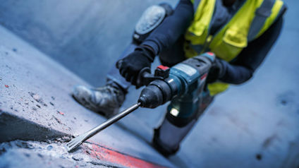 Person med skyddsväst använder en elektrisk bilmaskin för att bryta betong.
