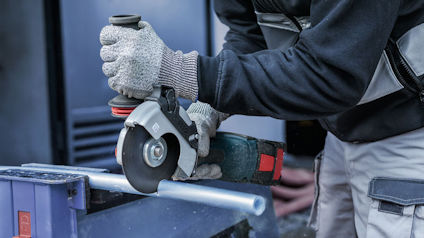 Person med handskar slipar metallrör med vinkelslip.