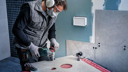 Person iklädd skyddsutrustning borrar hål i en skiva med en borrmaskin.