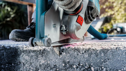 Cirkelsåg i användning på en betongyta, med skyddsskor synliga.