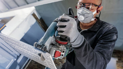 Person med skyddsmask och handskar använder en slipmaskin för att bearbeta metall.