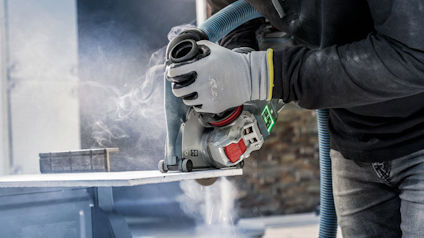 Person med handskar använder en vinkelslip på en vit yta. Damm och gnistor syns i luften.