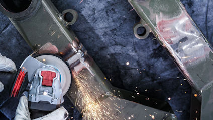 Person slipar metallrör med en vinkelslip, gnistor flyger.