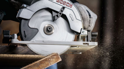Cirkelsåg i bruk, sågar en träplanka; träflisor flyger i luften.
