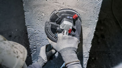 Person i handskar använder vinkelslip på betongvägg.