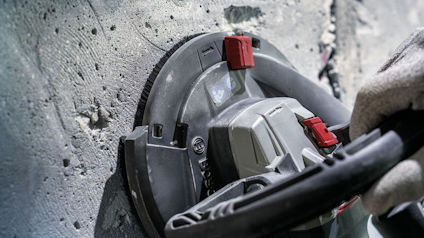 Hand som håller i en handhållen väggslipmaskin mot en betongvägg.