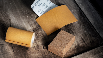 Slippapper, slipkloss och ett sandpapperblock på ett träbord.