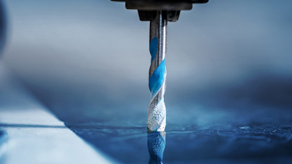 Närbild på en borr som borrar i en blå yta underifrån.
