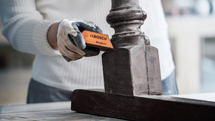 En person håller ett Bosch-verktyg och jobbar på ett brunt järnföremål.
