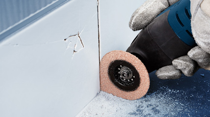 Hål i en vägg skärs med ett elverktyg med ett cirkelblad; hand i skyddshandske syns.