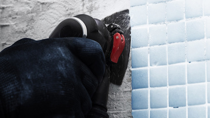 Hand i handske som använder ett verktyg för att bearbeta kakel på en vägg.