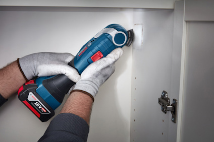 Person med handskar slipar insida av ett vitt skåp med en blå och röd sladdlös slipmaskin.