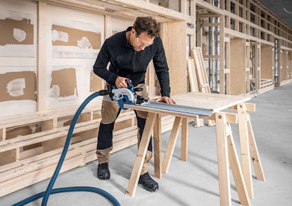 Person sågar en planka med en cirkelsåg i en byggnadsmiljö.