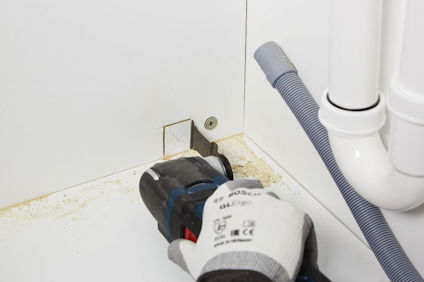 En person i vita handskar använder en elektrisk såg på en vit skiva intill PVC-rör och en böjlig slang.