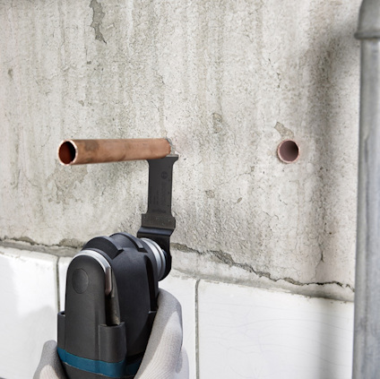 Verktyg skär en kopparrör mot en vägg med två hål.