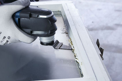 En person med arbetshandske använder ett verktyg för att skrapa bort färg från ett fönster med en oscillerande såg.