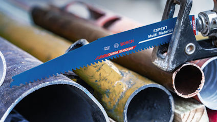 Blå Bosch sågblad märkt "Expert Multi Material" placerad på järnrör och rostiga metallrör i bakgrunden.