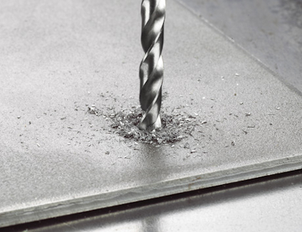 Borrspets borrar genom metallplåt, metallspån runt hålet.