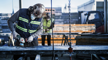 Arbetare med skyddsutrustning slipar metall med vinkelslip på byggarbetsplats.