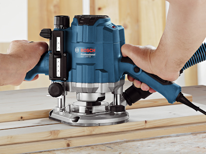 En blå och svart Bosch router används för att fräsa trä på en arbetsyta.