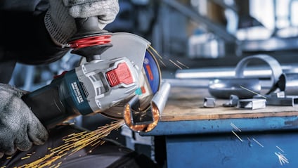 En person i handskar använder en vinkelslip på en metallstång, gnistor flyger från skärpunkten.
