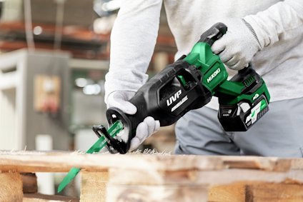 Person som använder en grön Hitachi eldriven tigersåg för att såga genom träplankor.