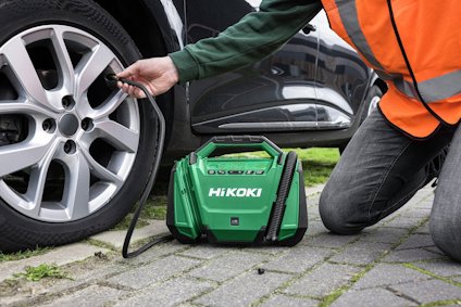 Person fyller luft i ett bildäck med en grön HiKOKI kompressor på en trottoar.