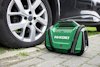 En grön HiKOKI-portabel kompressor bredvid ett bilhjul på gatsten.
