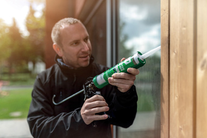 Man using a caulk gun to apply sealant to a wooden structure outdoors.